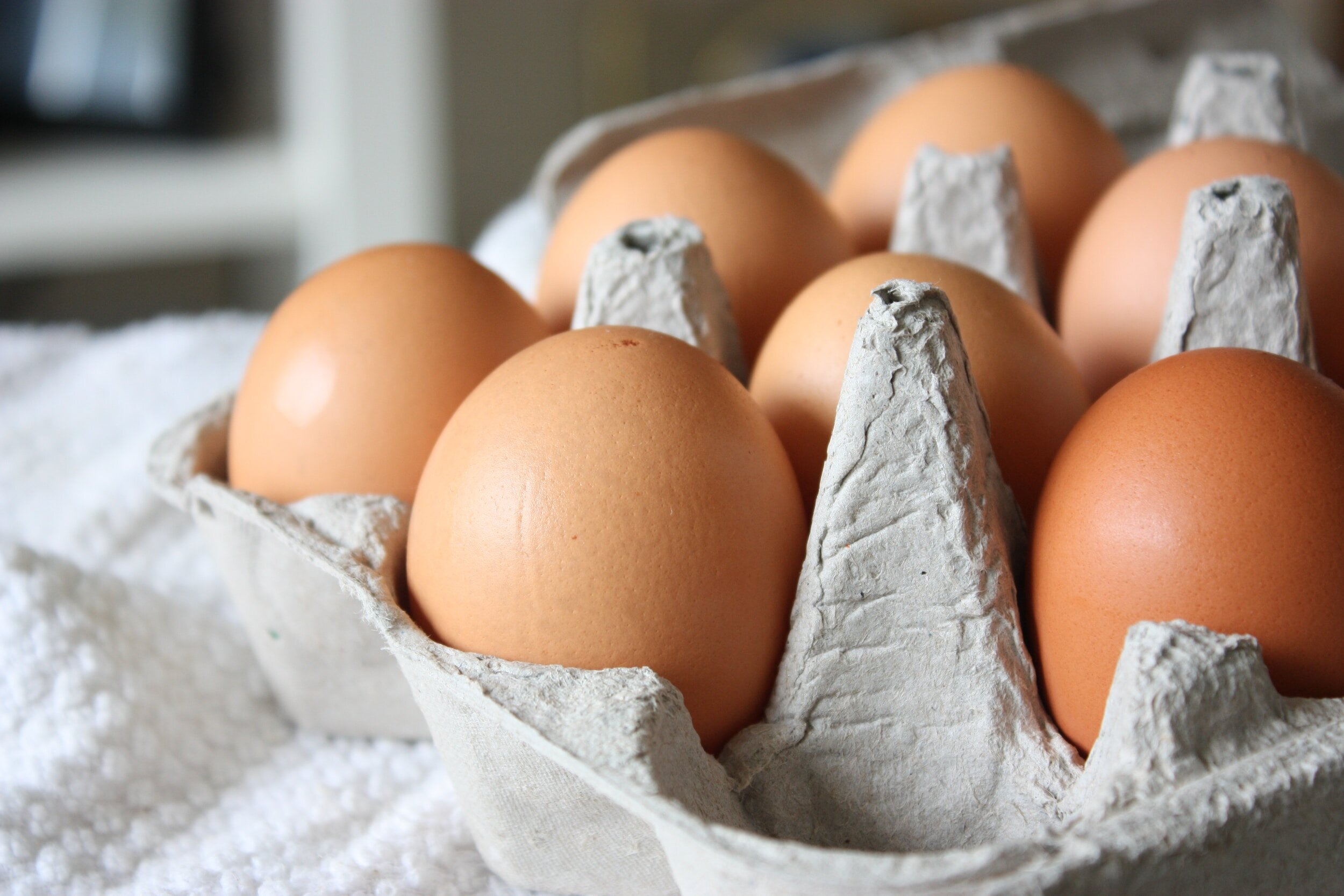 Fresh brown eggs in a cardboard carton, arranged neatly on a textured white surface, highlighting their smooth shells and natural color.
