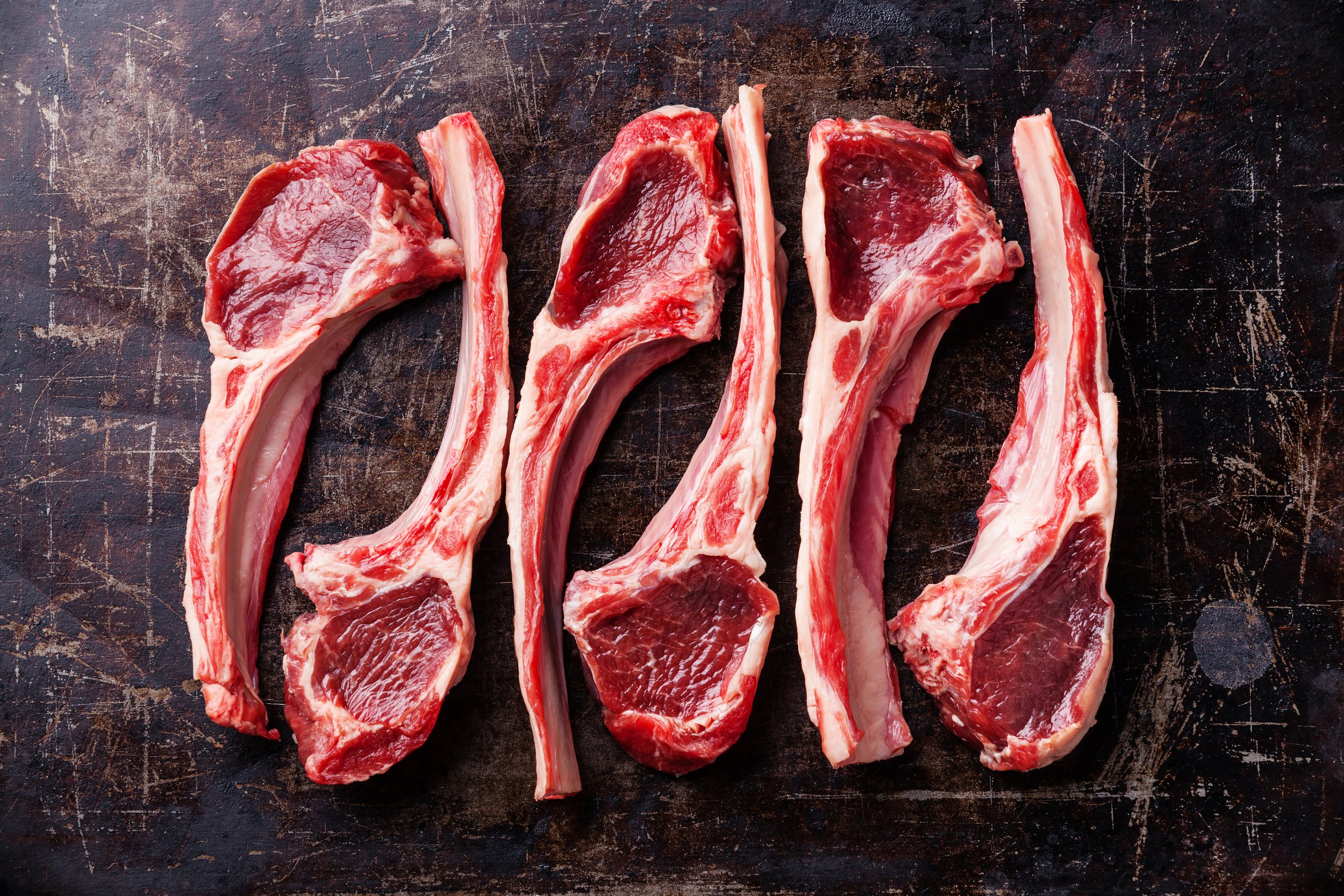 Four raw ribeye steaks displayed on a rustic wooden surface, showcasing their marbled texture and rich red color, ideal for grilling or roasting.